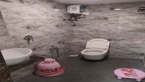 Een badkamer met een wastafel, toilet, douche en een klein roze krukje.