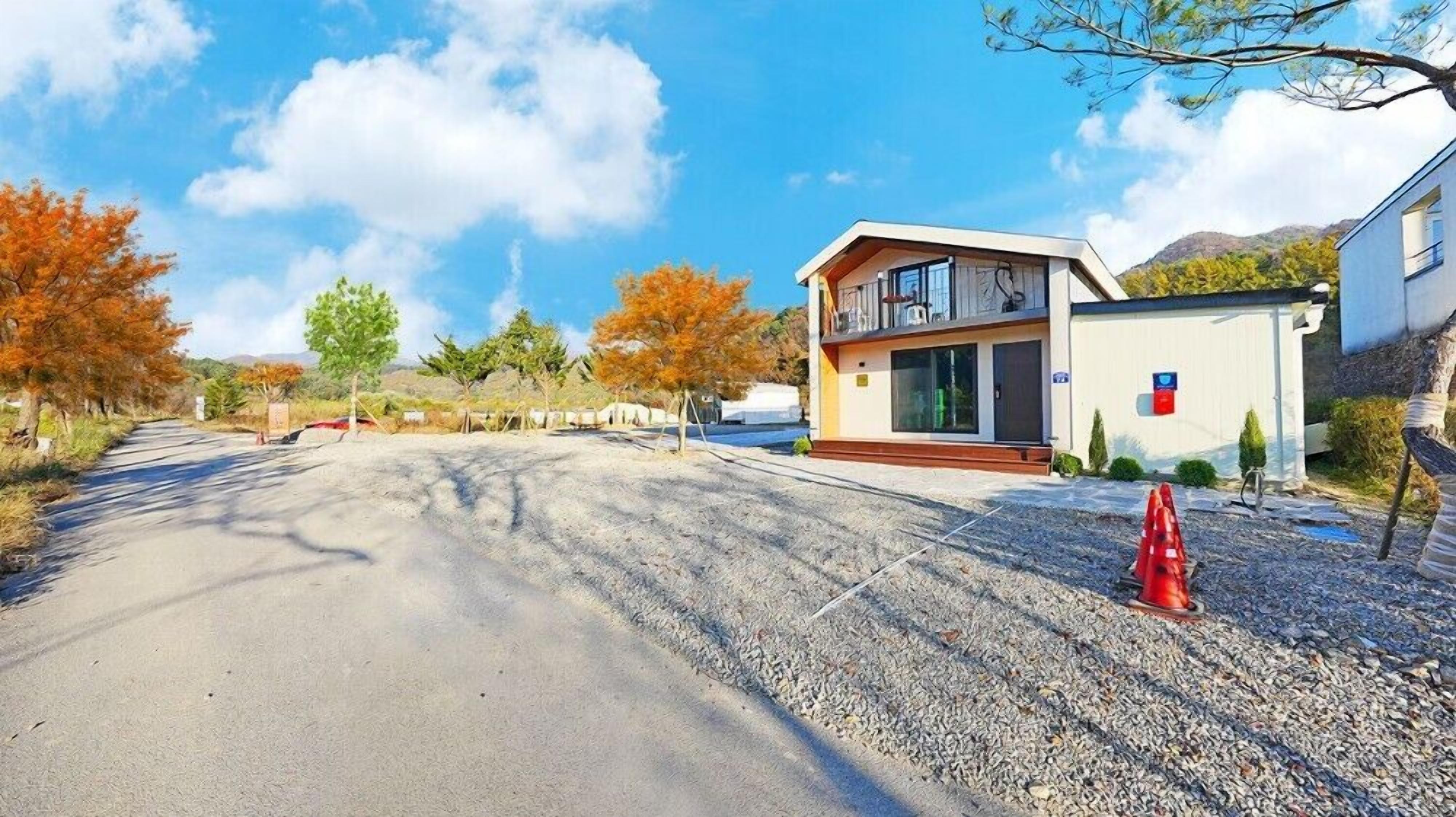 A modern two-story house with a balcony, a driveway, and a gravel path.