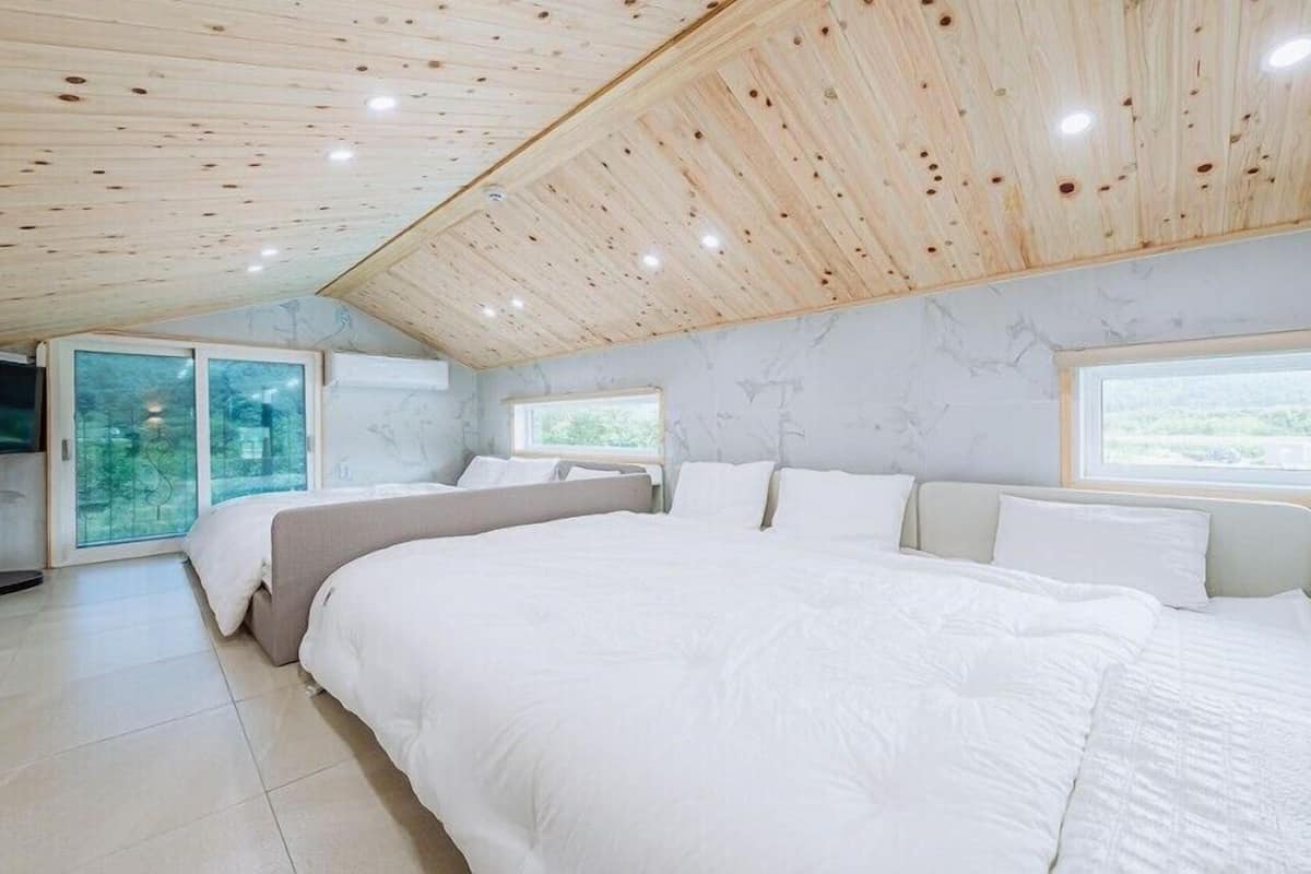 A bedroom with a large bed, a TV, and a window overlooking greenery.