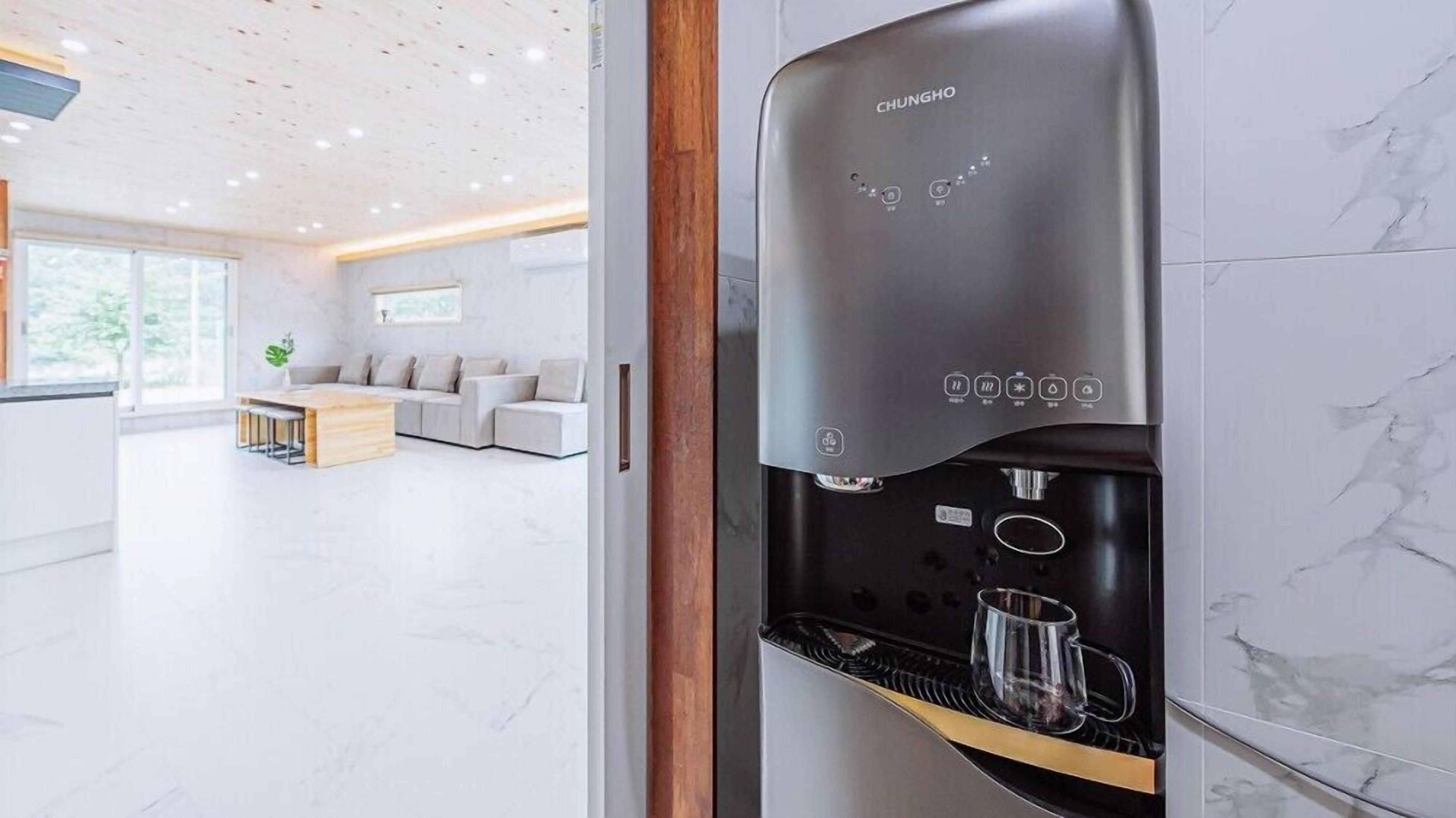A modern coffee machine in a hotel lobby with a minimalist design, a seating area with a sofa and a table, and a large window providing natural light.