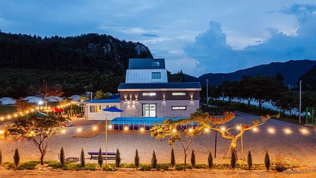 A modern hotel with a flat roof, a swimming pool, and a well-lit outdoor area with string lights. - jayeonsog gong gan (Gapyeong)