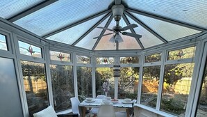 A conservatory with a table set for dining, surrounded by chairs, and a ceiling fan.