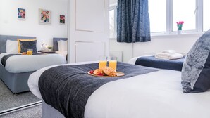 A hotel room with two beds, a window with curtains, a bedside table with a lamp, and artwork on the wall.