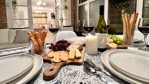 A dining table set with plates, cutlery, a bottle of wine, cheese, crackers, and grapes.