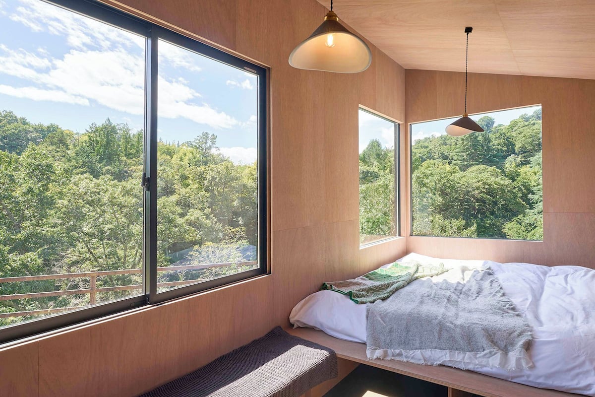 Ein Schlafzimmer mit großem Fenster, einem Bett, einem Nachttisch und einer Pendelleuchte.