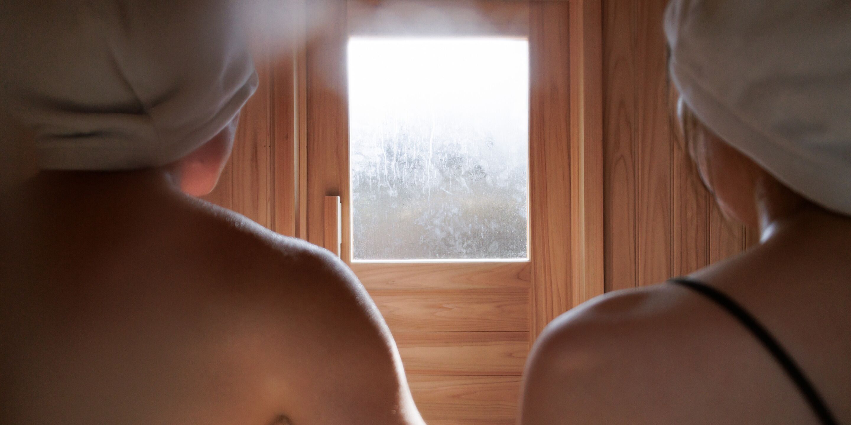 Two people with towels on their heads looking out of a wooden door.