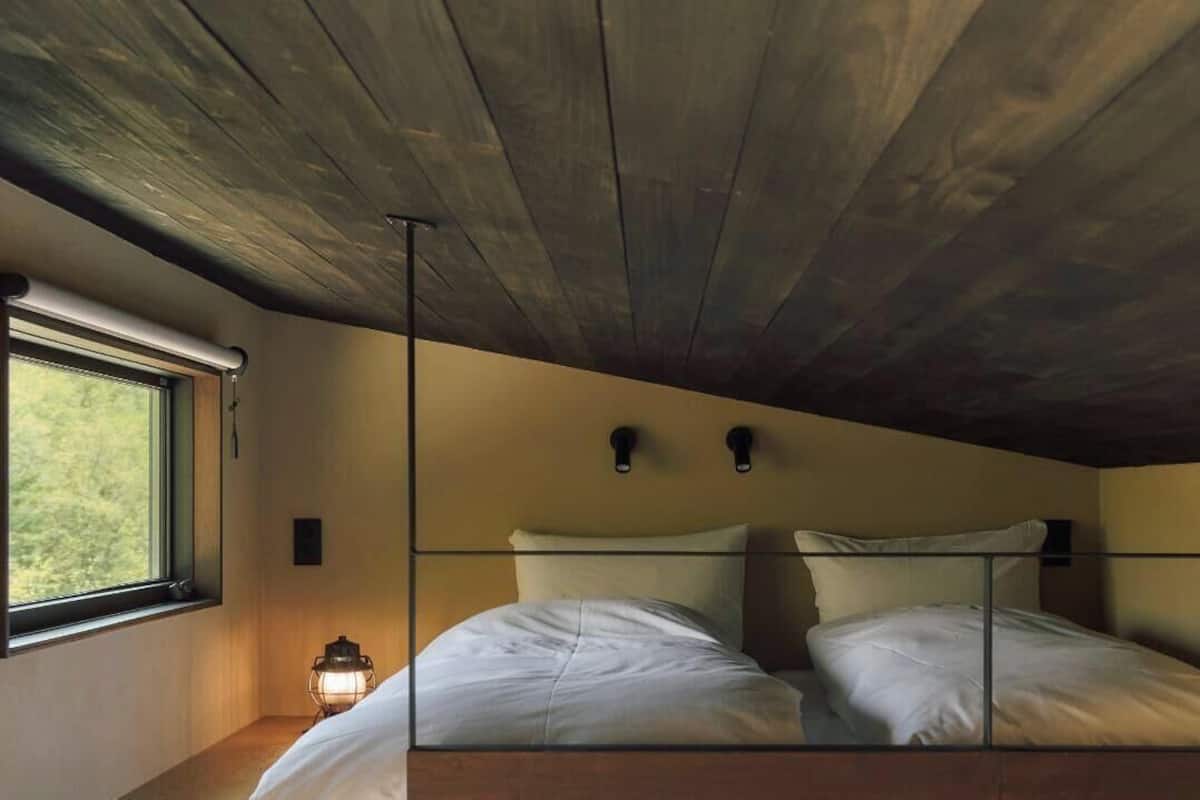 Ein Zimmer mit Holzbalkendecke, einem Bett mit weißer Bettwäsche, einem Fenster mit Blick und einer Wandleuchte.