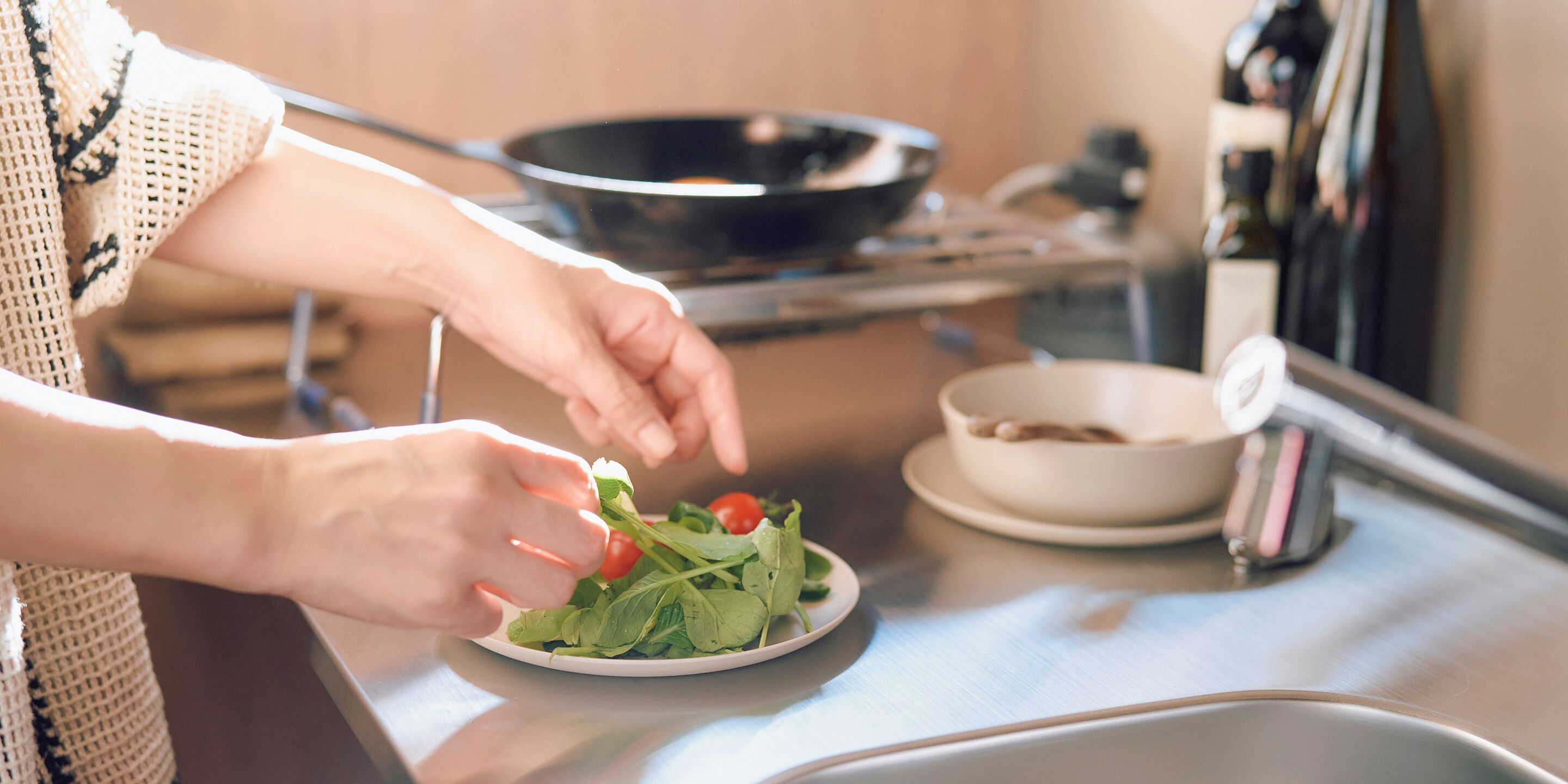 Une personne prépare une salade sur un plan de travail de cuisine, avec une assiette de légumes verts et de tomates à portée de main.