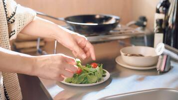 Une personne prépare une salade sur un plan de travail de cuisine, avec une assiette de légumes verts et de tomates à portée de main.