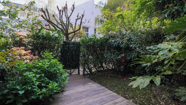 A wooden pathway leading through a lush garden with various plants and trees.