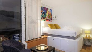A modern bedroom with a bed, a TV, a window with curtains, a painting, and a sign that reads "COU TEAUX".