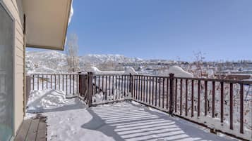Une terrasse enneigée avec une balustrade en bois, un ciel dégagé et un paysage montagneux en arrière-plan.