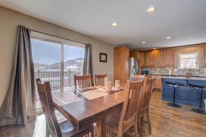 A dining area with a wooden table and chairs, a kitchen with wooden cabinets, and a view of a snowy landscape through large windows.