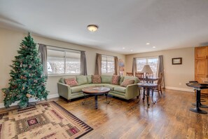Sala de estar com um sofá verde, uma mesa de centro redonda, um pinheiro de Natal e uma área de jantar com mesa e cadeiras.