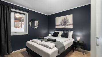 Une chambre à coucher avec un grand lit, une table de chevet avec une lampe, une fenêtre avec des rideaux et un miroir fixé au mur.