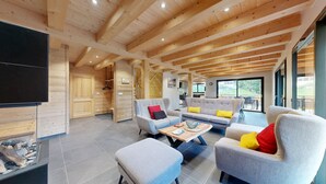 Un vaste espace de vie doté d’un plafond en bois, d’un téléviseur à écran plat et d’un ensemble de canapés.