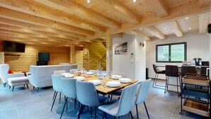 Un espace repas moderne avec un plafond en bois, des chaises à revêtement gris et une table à manger en bois, dressée pour six personnes.