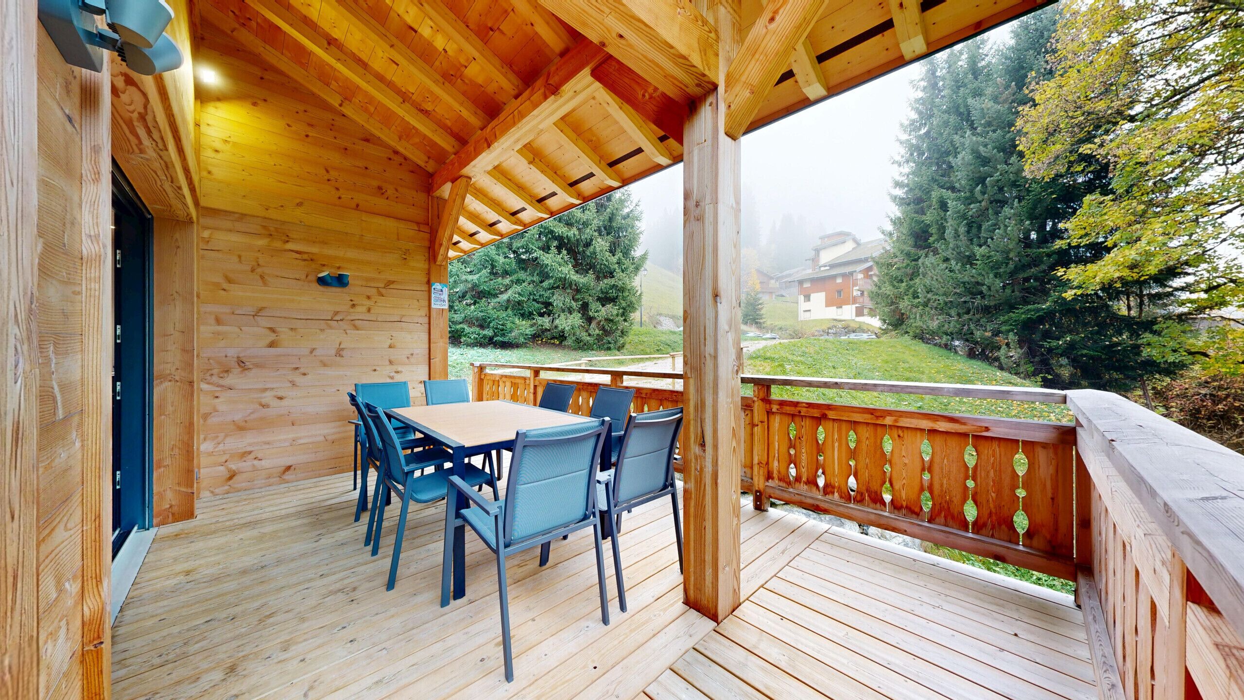 A wooden deck with a table and chairs, overlooking a forested area.