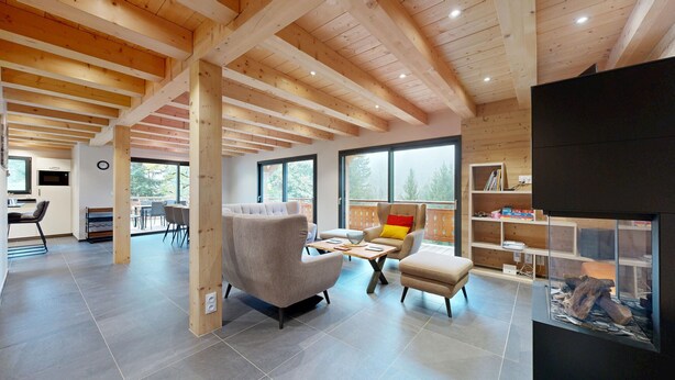 Un vaste espace de vie doté d’un haut plafond, de poutres en bois, d’une grande fenêtre, d’un canapé, d’une table basse et d’une bibliothèque.