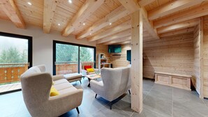 Un salon moderne avec des poutres en bois, de grandes fenêtres et un téléviseur.