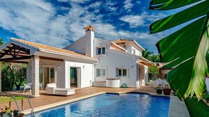 Ett modernt hus med en swimmingpool, en täckt uteplats och en trädgård.