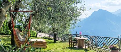 A hammock, wooden chairs, and a table set up on a grassy area with a mountain view.