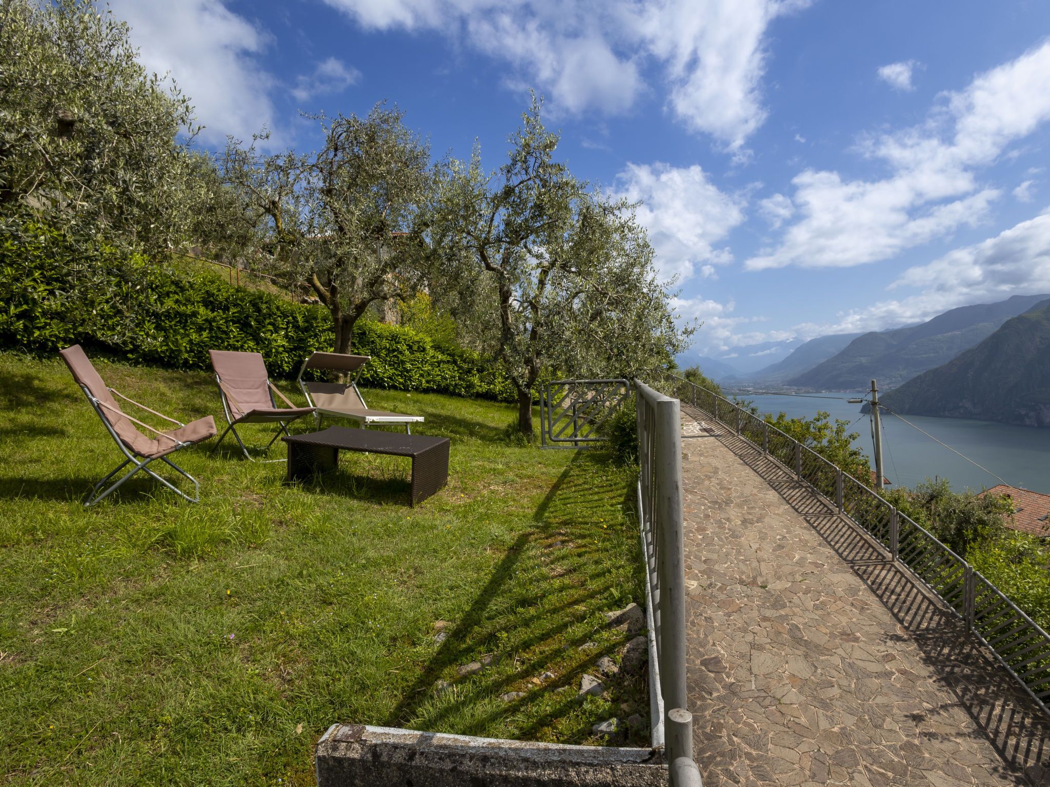 A terrace with outdoor seating, a stone pathway, and a view of a lake and mountains.