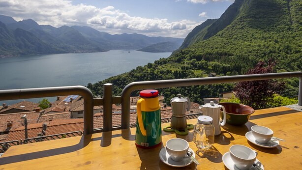 Una mesa con vista a un lago y montañas, una tetera, tazas y un termo.