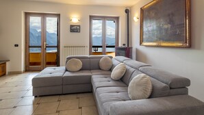 Una sala de estar con un sofá seccional grande, un cuadro en la pared y vistas a montañas a través de la puerta.