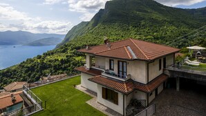 Una casa de dos pisos con techo de tejas rojas, un balcón y vistas a un lago y montañas.