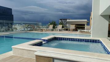 Una piscina al aire libre, sombrillas, sillones reclinables de piscina