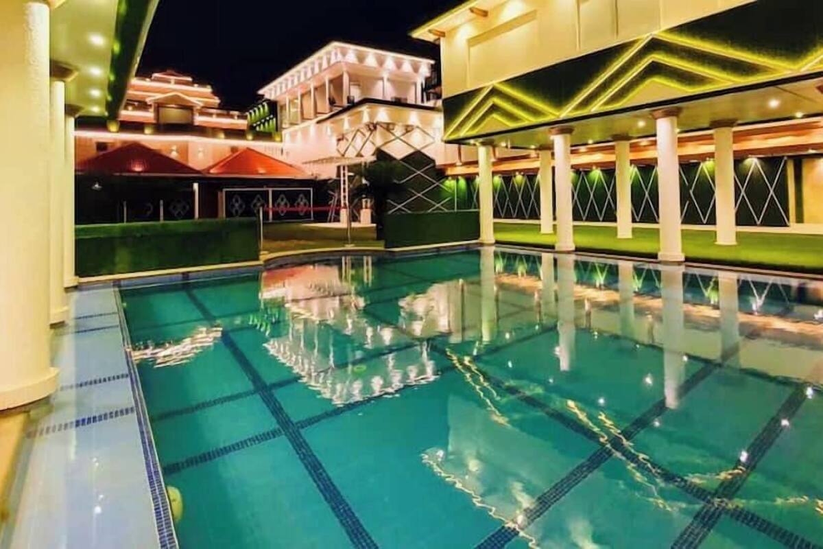 A swimming pool with clear water, surrounded by a building with a modern design and a covered area in the background.