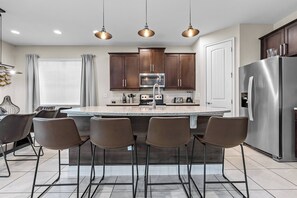 Welcome to this stylish kitchen featuring rich brown cabinetry and sleek stainless steel appliances. Enjoy casual dining at the modern bar under warm pendant lights, perfect for culinary creativity and social gatherings.