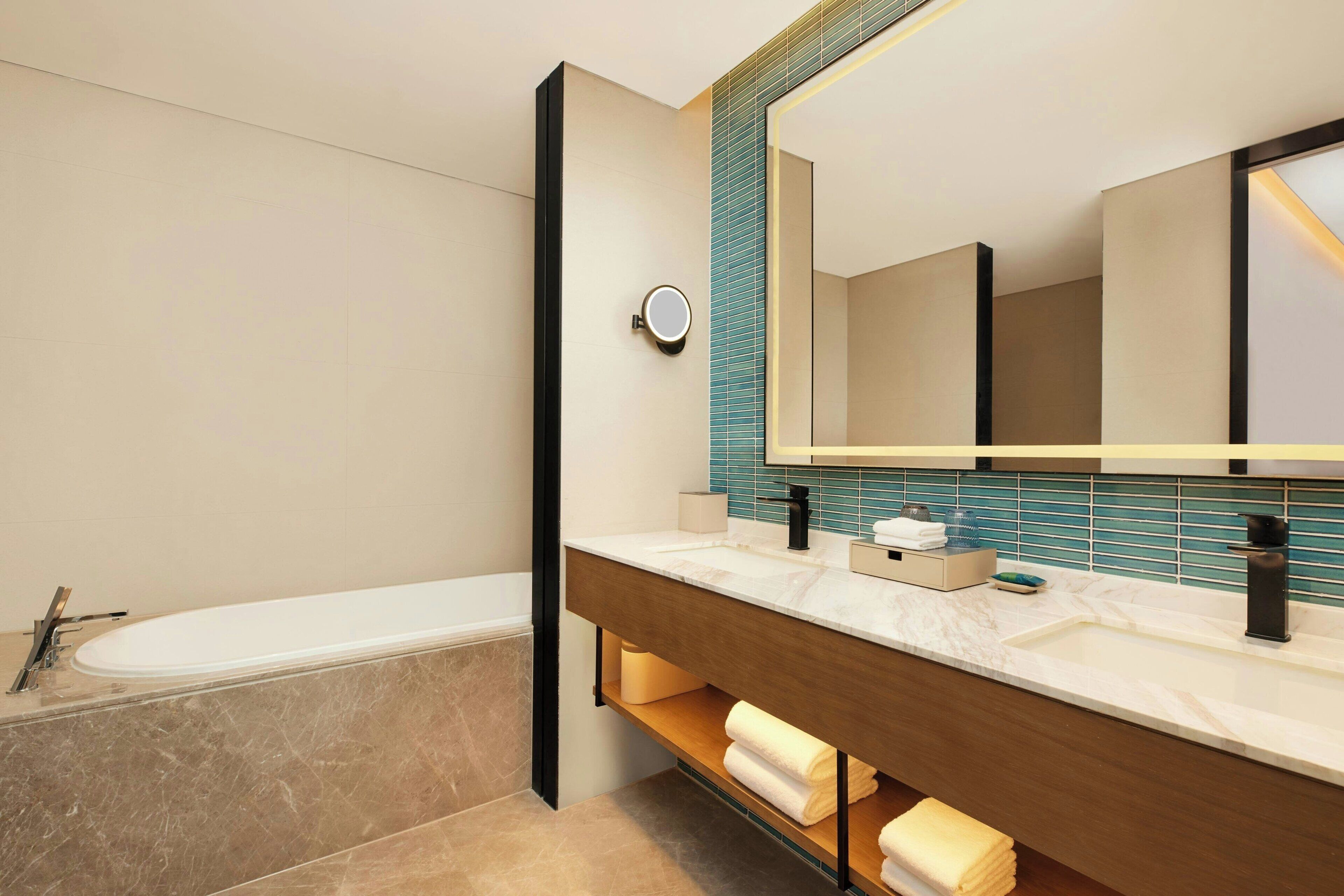 A modern bathroom with a bathtub, a large mirror, and a vanity with a sink.