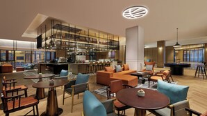 Un hall d’hôtel moderne doté d’un bar, de différents espaces de détente et d’une table de billard.