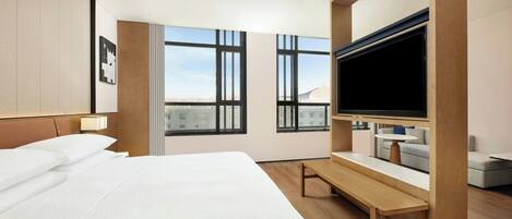 Camera d'albergo con un letto grande, una TV, una panca e ampie finestre con vista sulla città.
