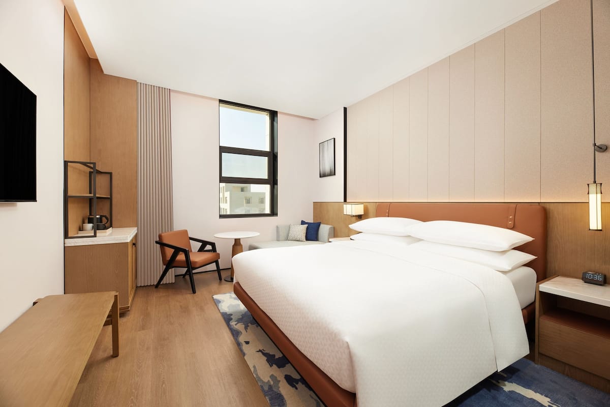 Ein modernes Hotelzimmer mit einem großen Bett, einem Schreibtisch, einem Sessel, einem kleinen Tisch und einem Fernseher.