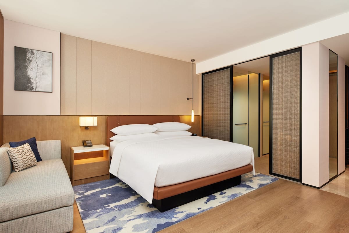 Ein modernes Hotelzimmer mit einem großen Bett, einer Couch, einem Nachttisch und einem Schiebetürenschrank.