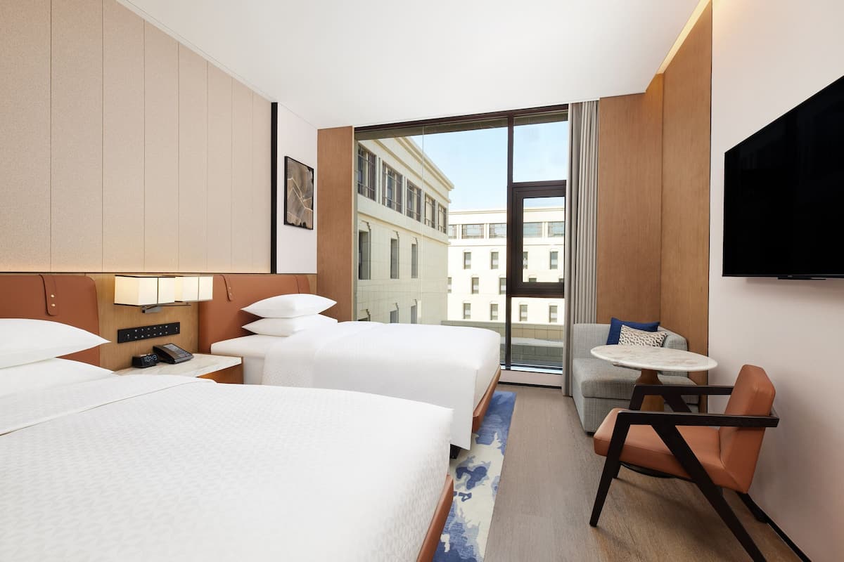 Ein Hotelzimmer mit zwei Betten, einem Fernseher, einem kleinen Tisch und einem Sessel.