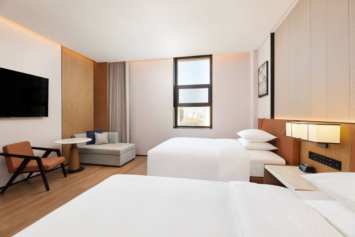 Ein Hotelzimmer mit Bett, einer Sitzecke, einem Sessel, einem kleinen Tisch, einem Fernseher und einem Fenster mit Blick.