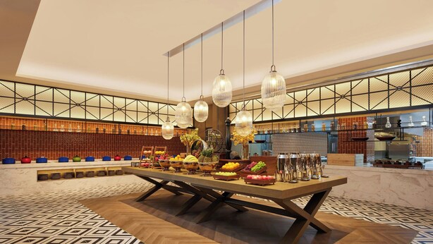 Un vaste espace dédié à la salle à manger, avec une longue table, des luminaires suspendus et une variété de fruits et de boissons.