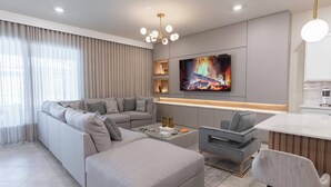 A modern living room with a grey sectional sofa, a coffee table, a TV mounted on the wall, and a small bar area. - 10BR house sleeps 22 with game room (Clermont)