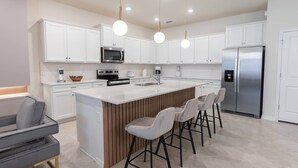 A modern kitchen with white cabinets, a stainless steel refrigerator, a built-in oven, and a central island with bar stools. - 10BR house sleeps 22 with game room (Clermont)