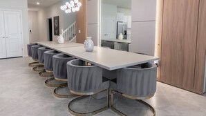 A modern kitchen with a long countertop, grey bar stools, and a chandelier. - 10BR house sleeps 22 with game room (Clermont)
