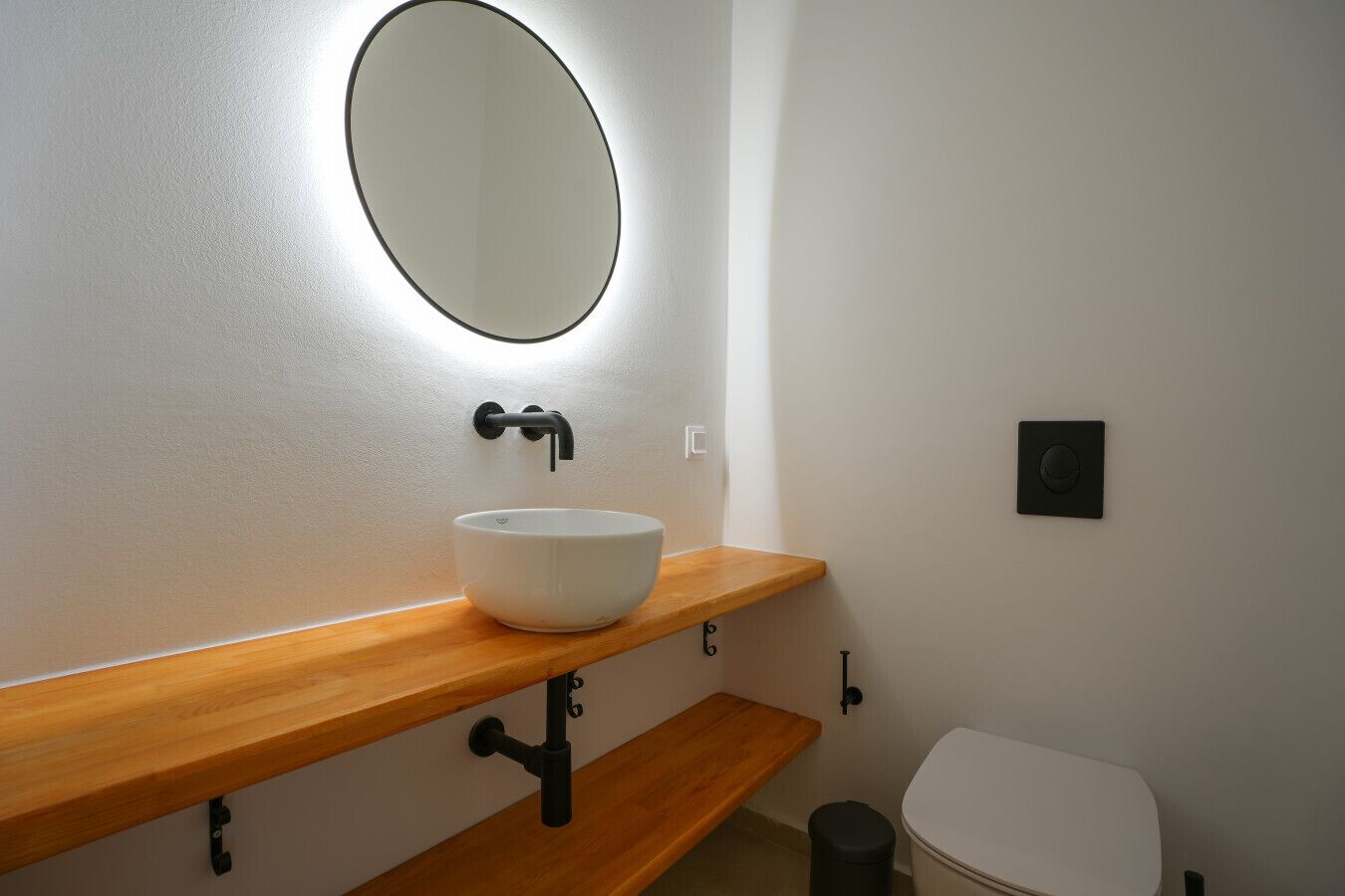 A bathroom with a white sink, wooden countertop, and a round mirror.
