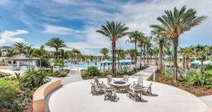 Zona de piscina en un resort, con un espacio de estar circular, palmeras y cielo despejado.