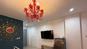 A modern bedroom with a chandelier, a TV, a refrigerator, and a unique wall decoration.