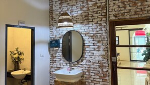 A bathroom with a brick wall, a sink, a mirror, and a toilet.