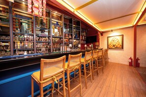 Una zona de bar con varias estanterías llenas de botellas, un televisor montado en la pared y varios taburetes de madera.