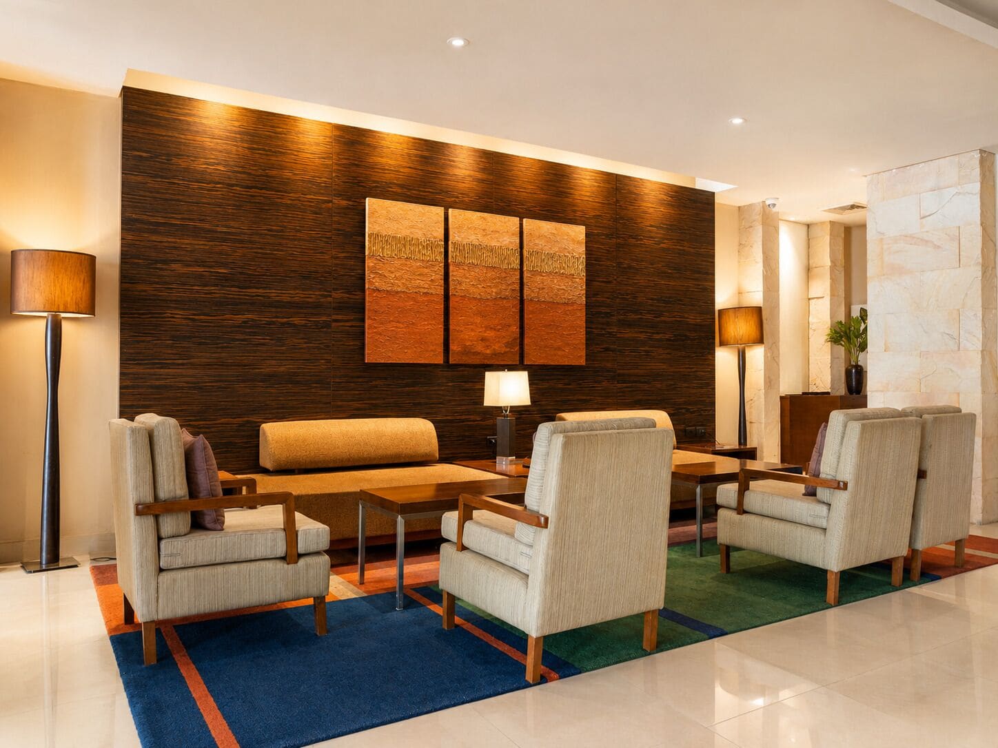 Un moderno vestíbulo con un panel de acento de madera, un sofá, sillones, una mesa de centro y dos lámparas de pie.